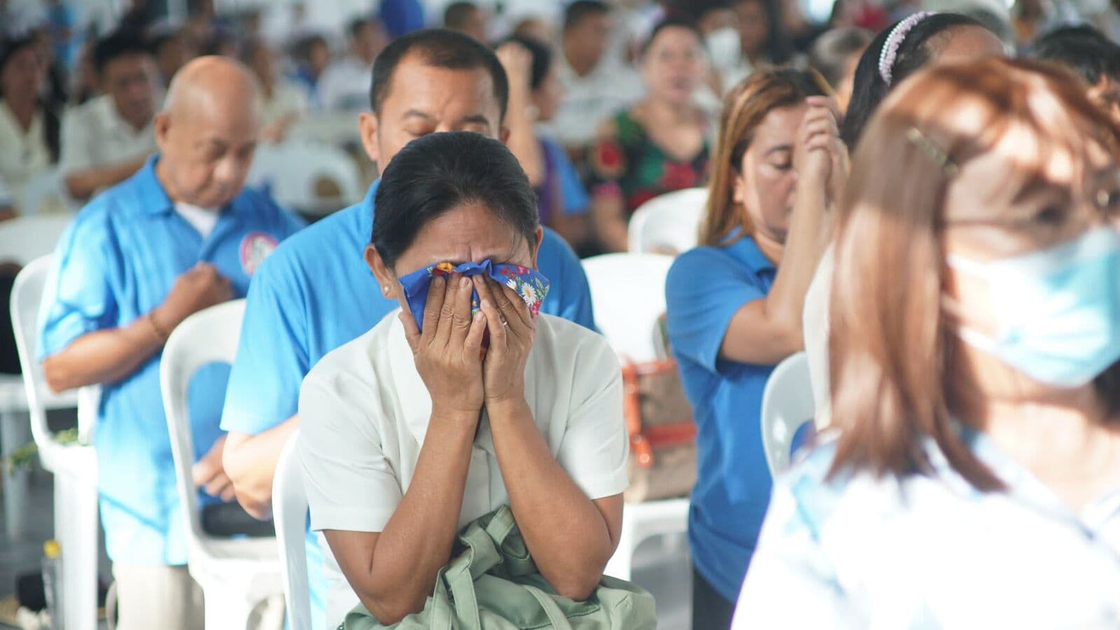 A woman covering her face with a handkerchief as she prays among a crowd