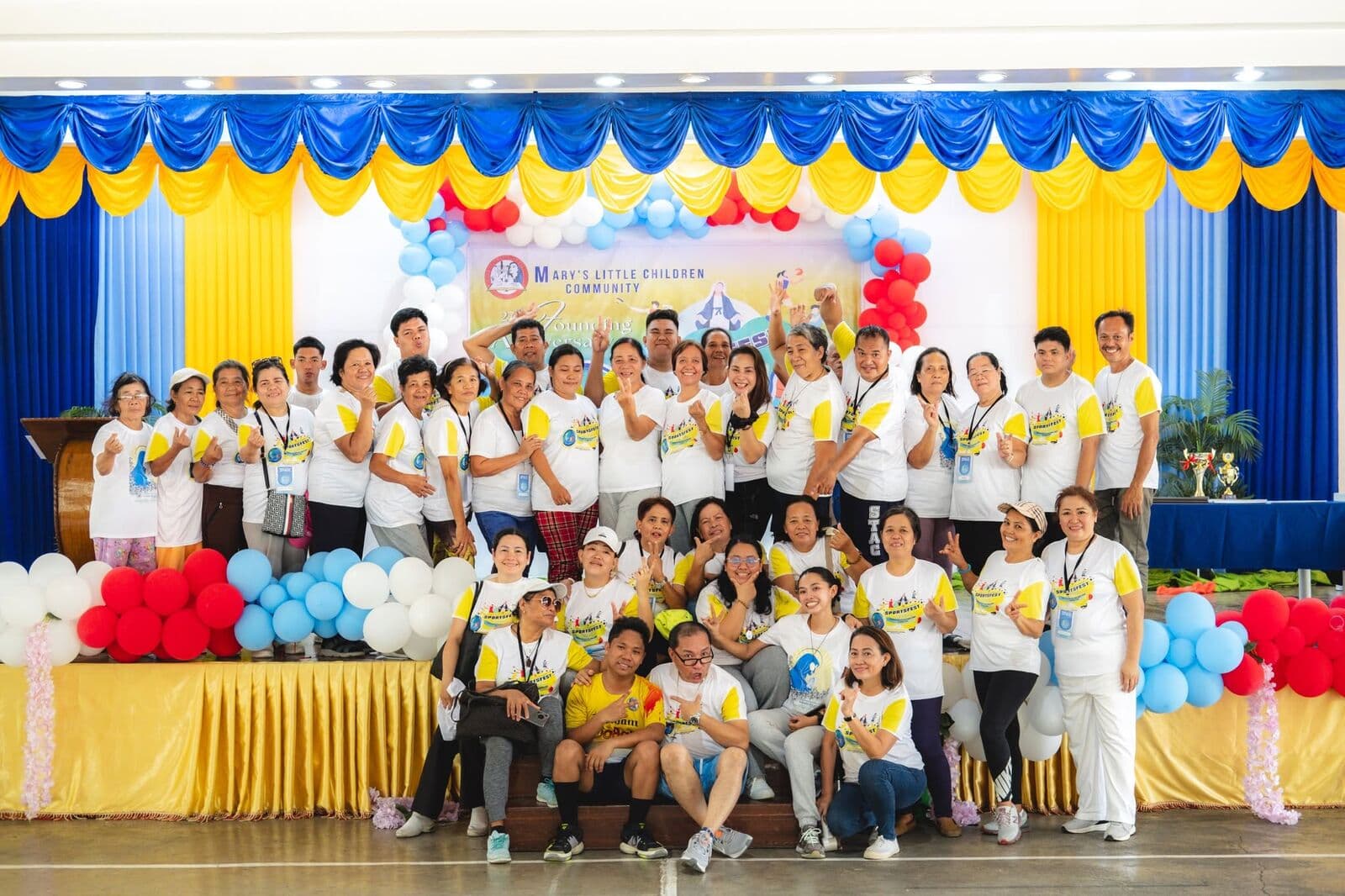 A large group of members gathered on a stage decorated with balloons