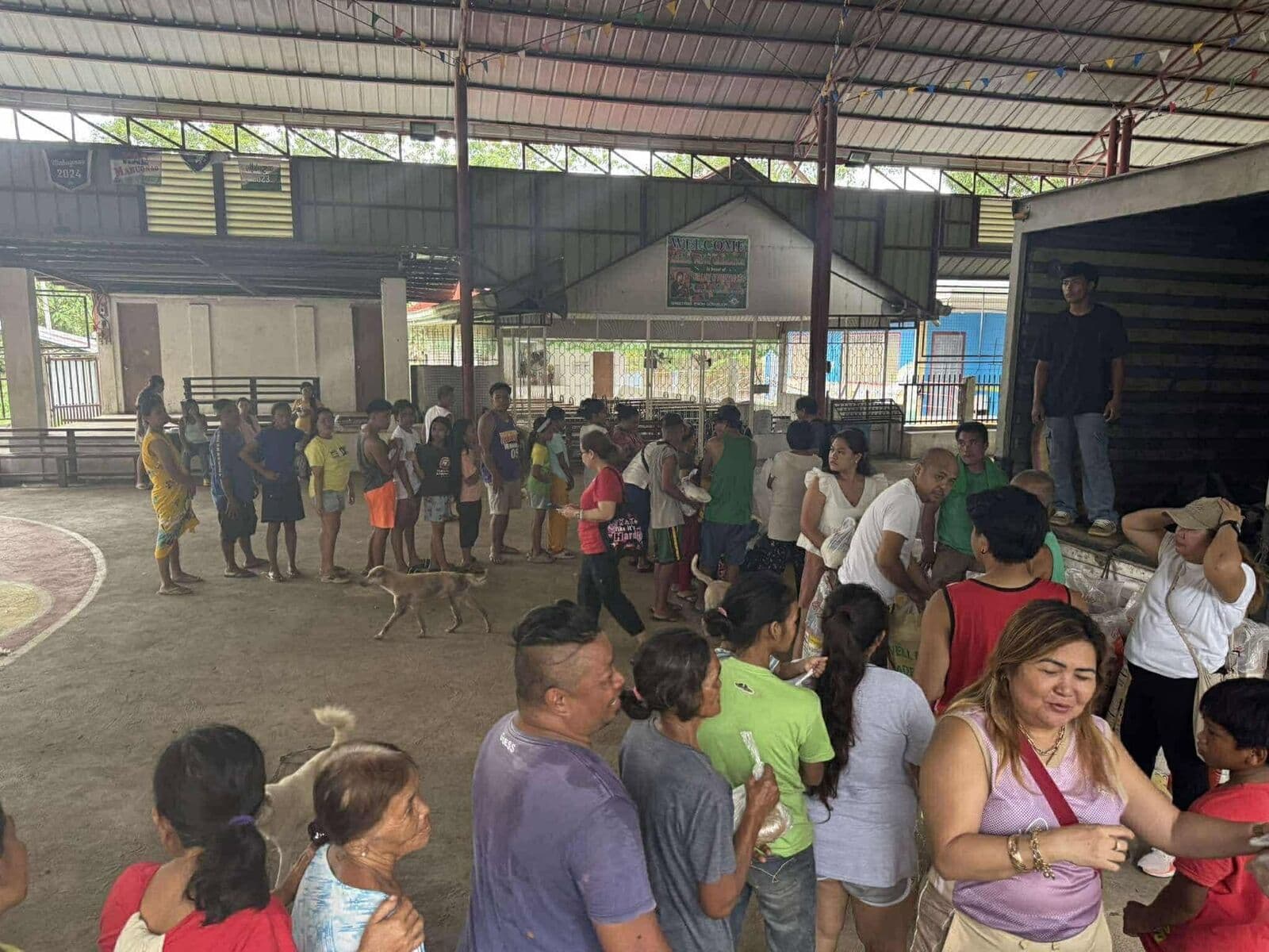 A crowd lining up on a covered court to receive relief goods