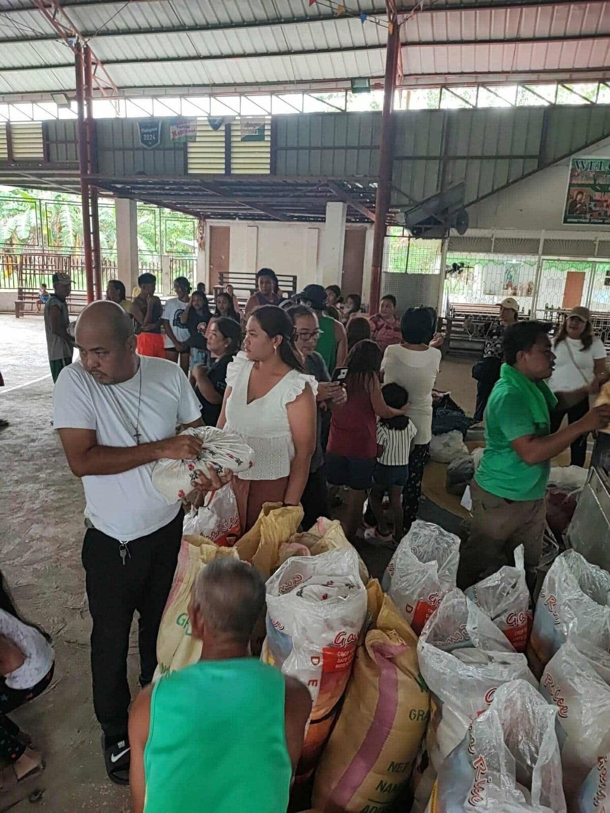 A volunteer handing out sacks of rice and supplies to people waiting on a covered court