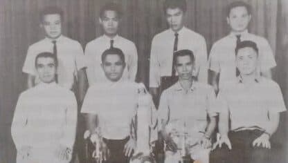 An old group photograph of eight young men in white shirts and ties